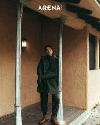 Model Jiaxuan Yang standing on a porch wearing a dark parka coat and brown leather boots for Arena Homme+ Korea.