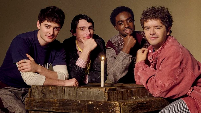 Four young male actors seated behind a wooden crate with a lit candle for British GQ photographed by Grace Difford