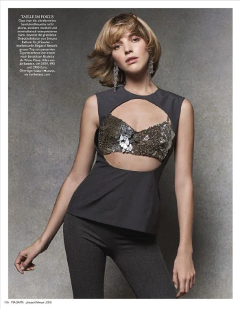 Editorial fashion shot of a female model in gray, sleeveless cut-out top and pants, adorned with sparkly sequins, against gray backdrop.