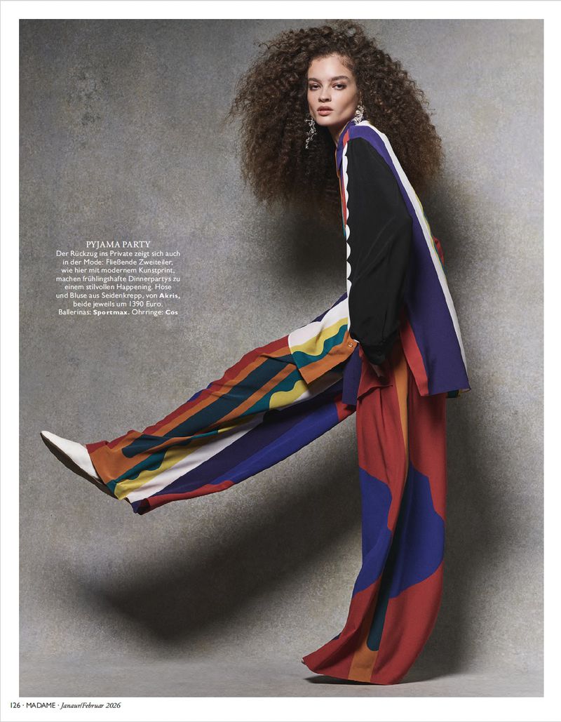 Model with voluminous curly hair in a vibrant multicolored colorblocked matching suit posing against a textured grey studio backdrop.