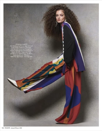 Model with voluminous curly hair in a vibrant multicolored colorblocked matching suit posing against a textured grey studio backdrop.