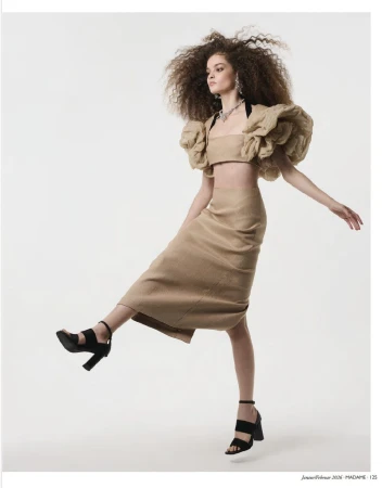 Fashion editorial shot of a woman in a beige crop top, skirt, and black high heels striking a pose in a studio setting.