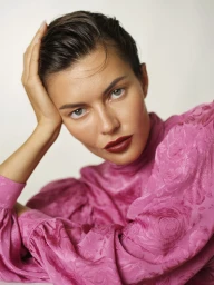 Close-up beauty portrait of a woman with slicked hair wearing bold dark red lipstick and a textured fuchsia pink puff-sleeve blouse.