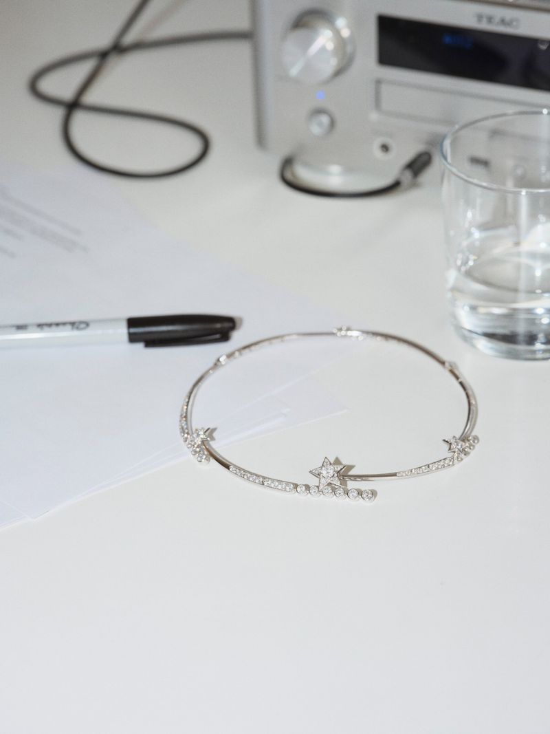 Elegant star-motif choker on a white surface alongside a pen, paper, and glass of water with a stereo receiver in the background.