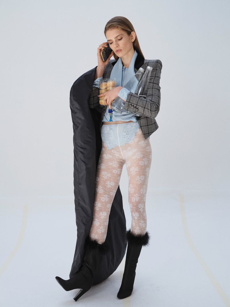 Fashionable woman wearing blazer, lace tights, and boots while talking on a cell phone and holding water bottles and snacks.