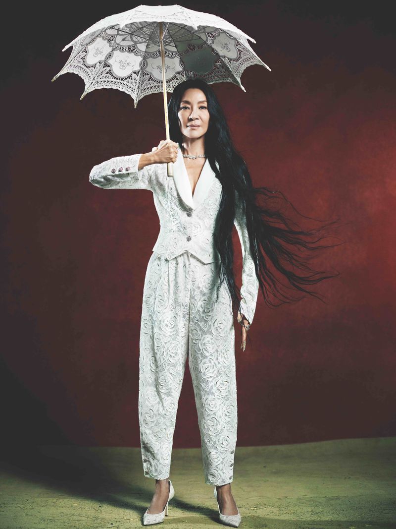 Elegant woman in a white lace suit holding a white lace umbrella against a red background. Studio shot, full-length portrait.
