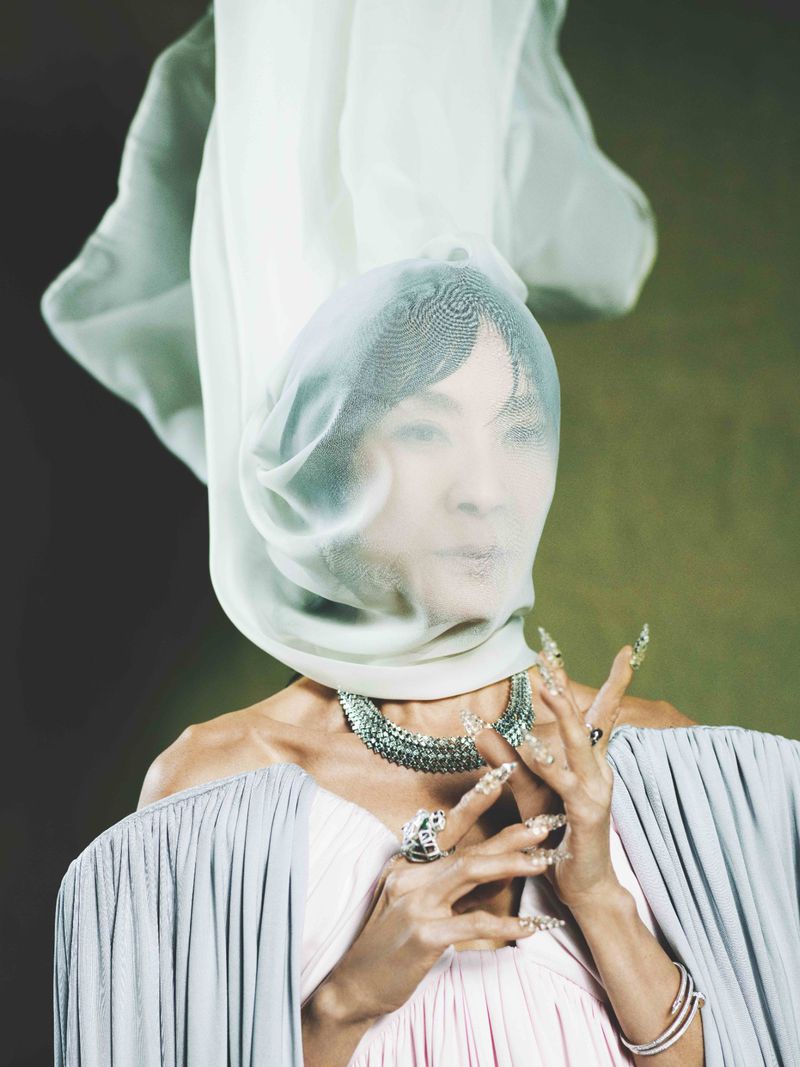 Portrait of an adult female wearing an elaborate veil, gown, and jewelry, posing in front of a green backdrop in a studio setting.