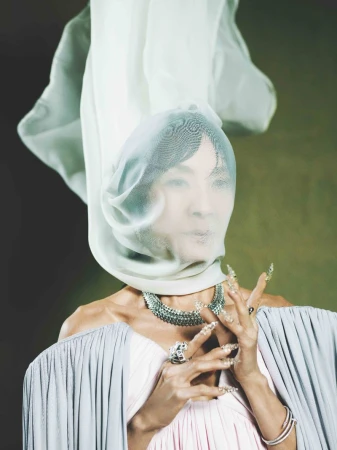 Portrait of an adult female wearing an elaborate veil, gown, and jewelry, posing in front of a green backdrop in a studio setting.