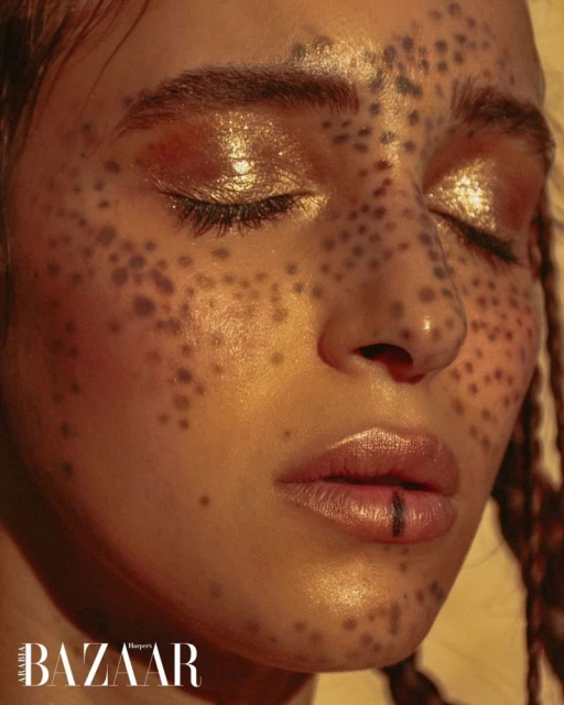 Close-up beauty portrait of a young adult woman with a closed-eye expression, freckle-like makeup, and light-brown braids.