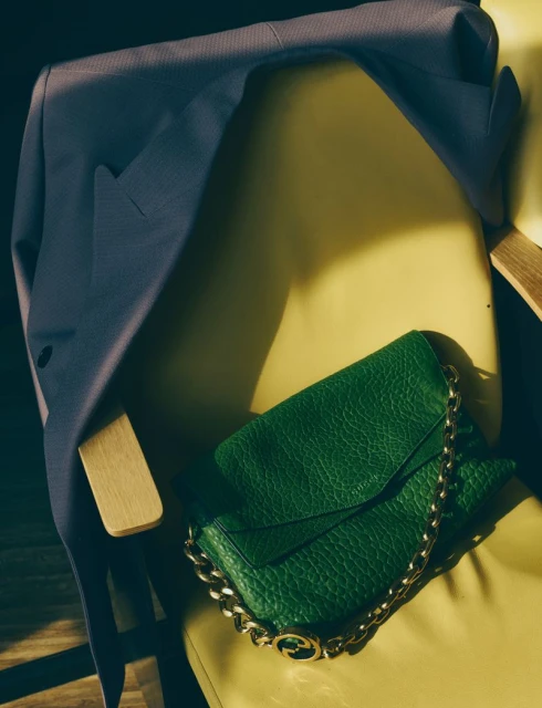 Fashion shot featuring a blue suit jacket draped on a yellow chair, with a green Gucci purse with a gold chain and logo.