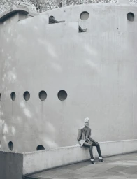 A model seated on a concrete wall outdoors against a large building exterior with circular windows for Grazia International