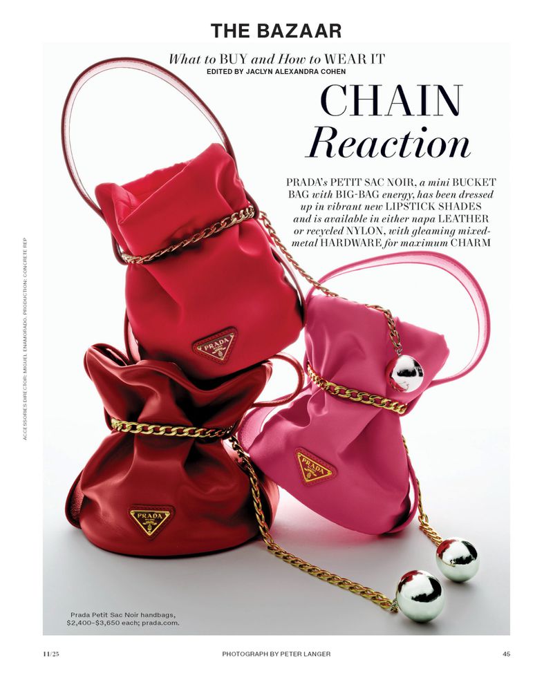 Fashion editorial featuring a stack of colorful Prada mini bucket bags in red and pink, accented with gold chain straps and metallic accents.