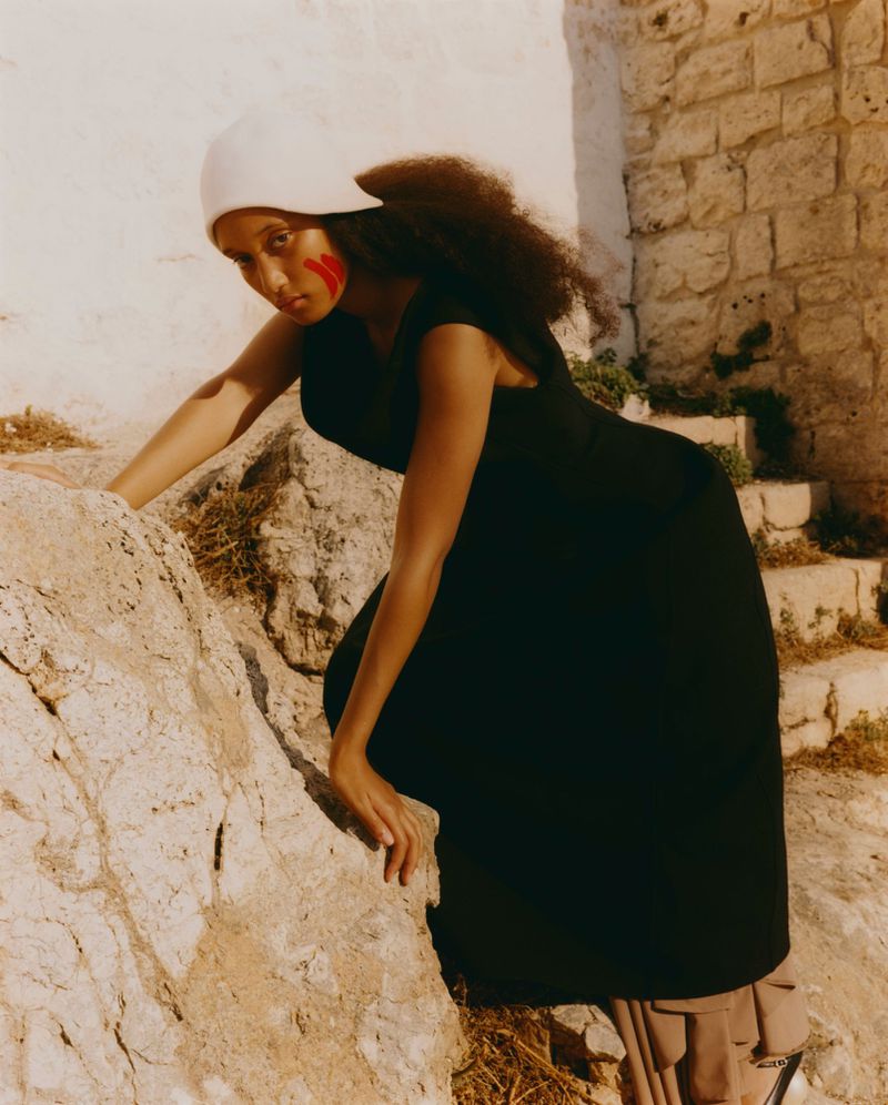 Model wearing a black dress and white cap climbing rocky stone steps outdoors for L'Officiel Singapore