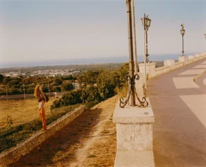 Model Alice Amankwah standing on a low stone wall overlooking a sunlit countryside landscape in Ostuni for L'Officiel Singapore.