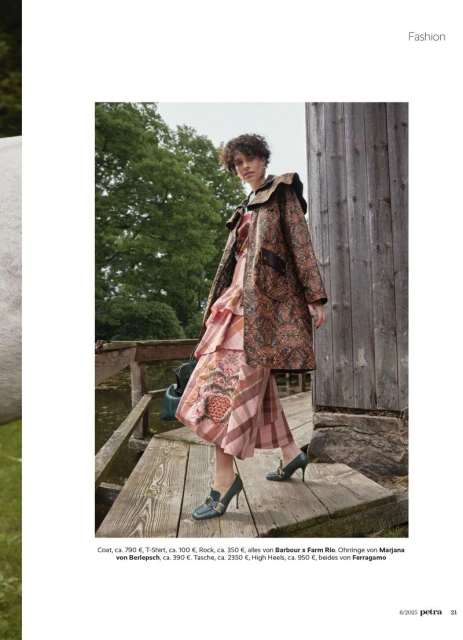 Fashionable woman in patterned coat and dress walks on wooden path surrounded by trees and greenery, captured in a medium outdoor shot.