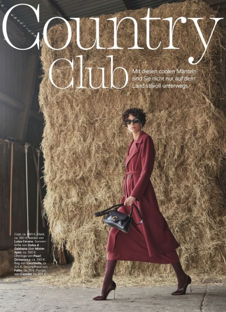 A woman in a maroon coat and sunglasses stands in a barn in front of a large hay bale, advertising Country Club fashion.