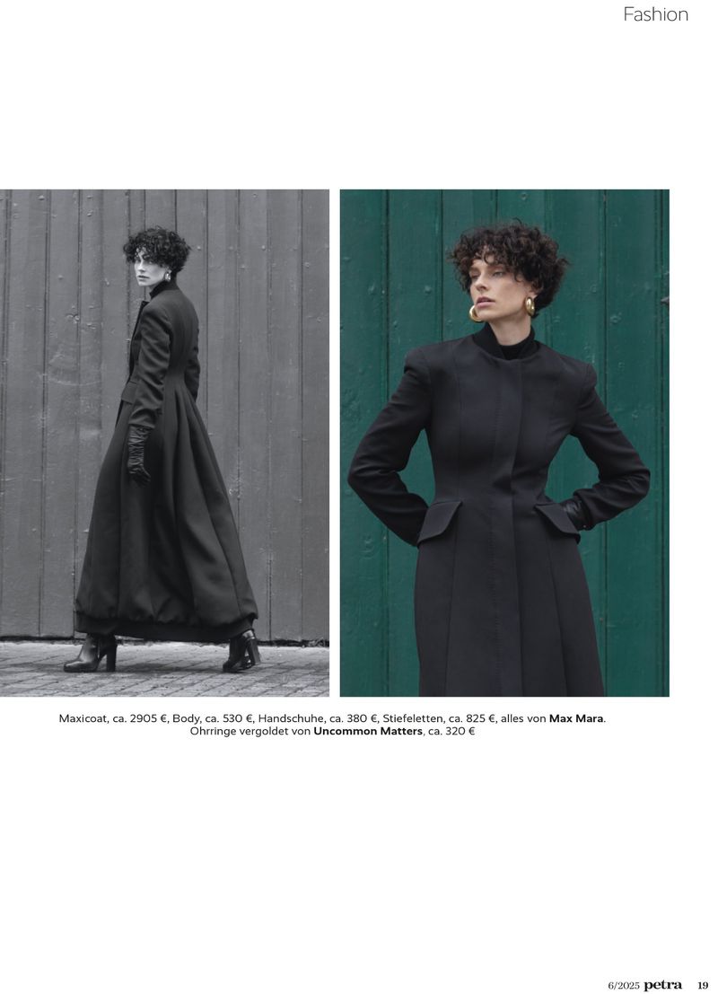 A fashion editorial presents a curly-haired woman in a long black coat against a muted wooden background and green wall, creating a minimalist aesthetic.