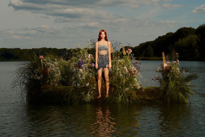 Young woman in matching crop top and skirt posing on a lush floral platform on a lake in an outdoor fashion editorial shoot.