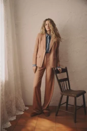 Model standing next to a wooden chair wearing a peach suit and blue shirt against a textured plaster wall