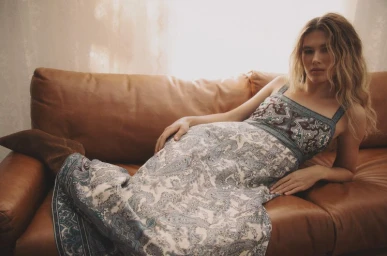 Model Meg Dmitruk in a blue and white paisley maxi dress reclining on a brown leather sofa for Veronica Beard.