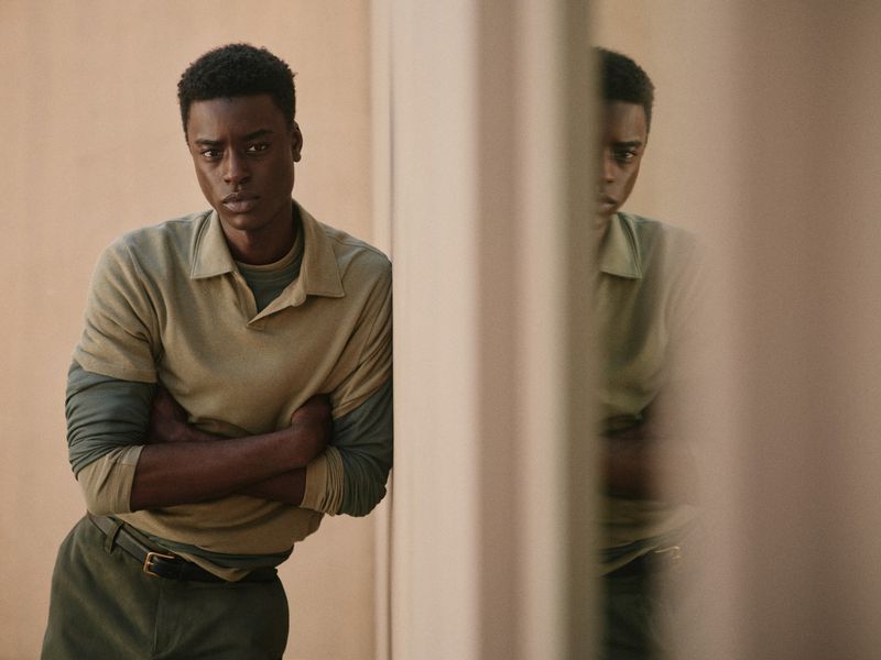 Portrait of a serious African-American male model with arms crossed, wearing a polo shirt, gazing at the camera indoors.