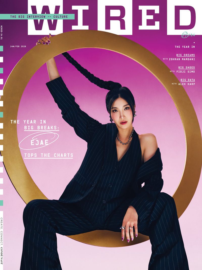 Magazine cover featuring a woman with long braided hair, wearing a pinstripe suit, posing with a gold ring prop against a purple backdrop.