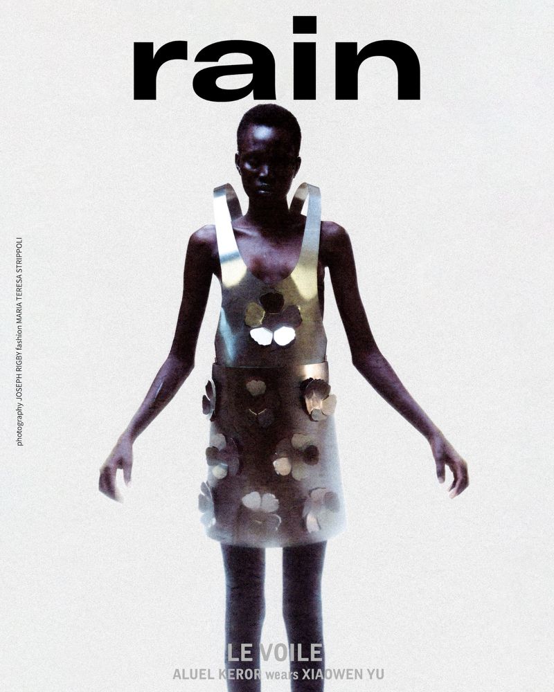 A dark-skinned fashion model poses in a glossy metallic dress with floral accents, set against a light background with ‘rain’ text above.
