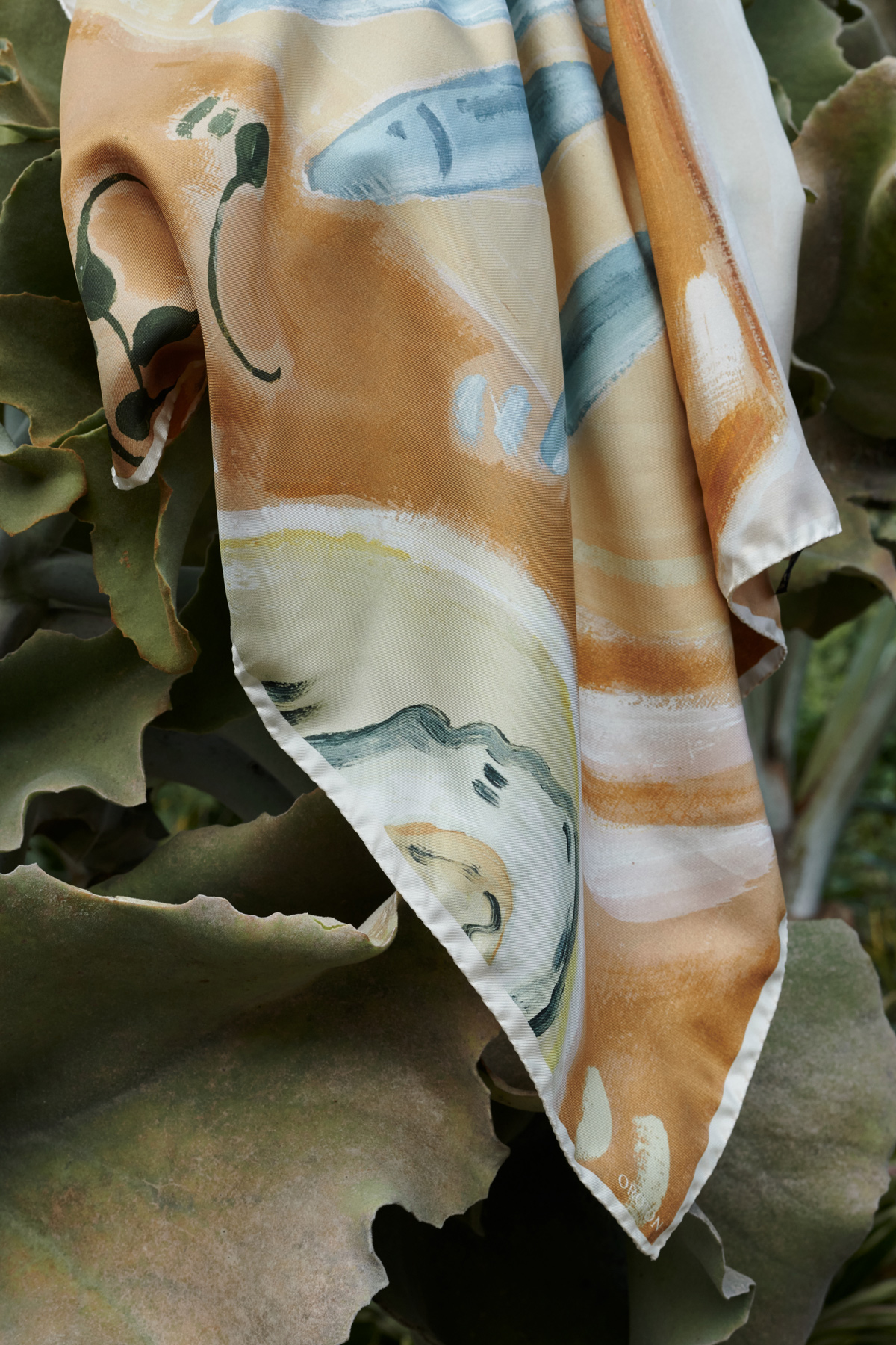 Artistic patterned scarf draped against lush green foliage, creating a blend of natural and textile artistry in outdoor setting.