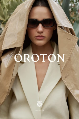 Model wearing dark sunglasses and a beige coat draped over her head for the Oroton Penfold Scarf Project campaign.