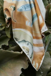 Oroton silk printed scarf draped over broad green leaves outdoors in natural light