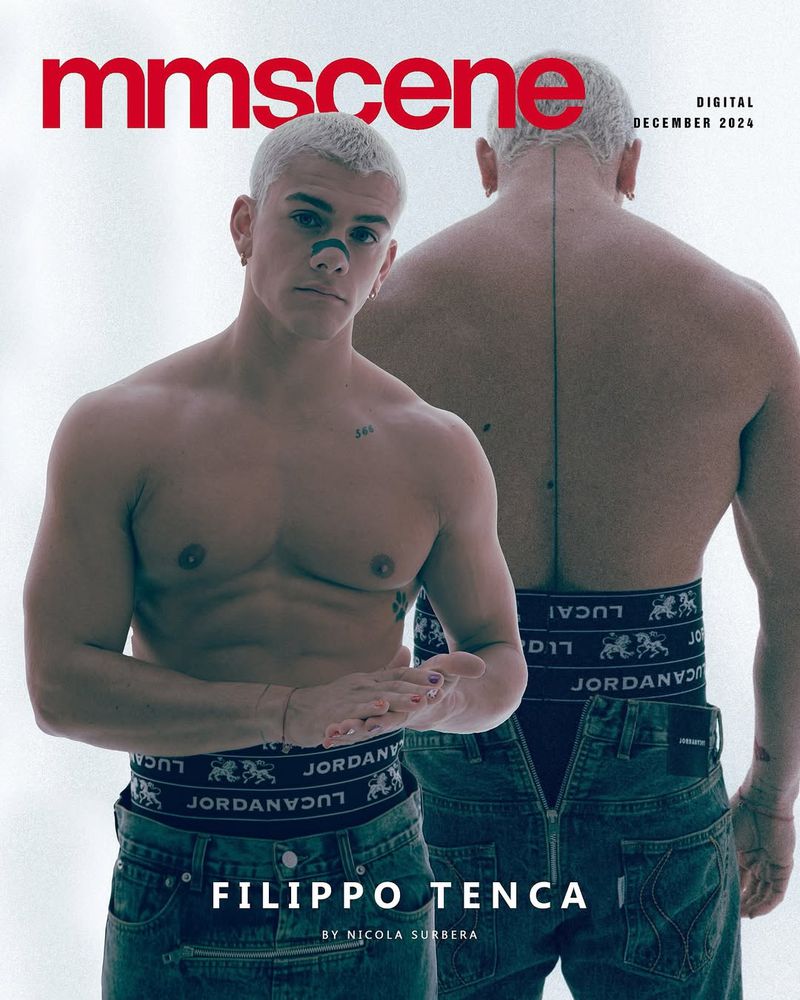 Magazine cover featuring a shirtless male model with short white hair and a tattoo, wearing jeans. Another partially visible man behind him.