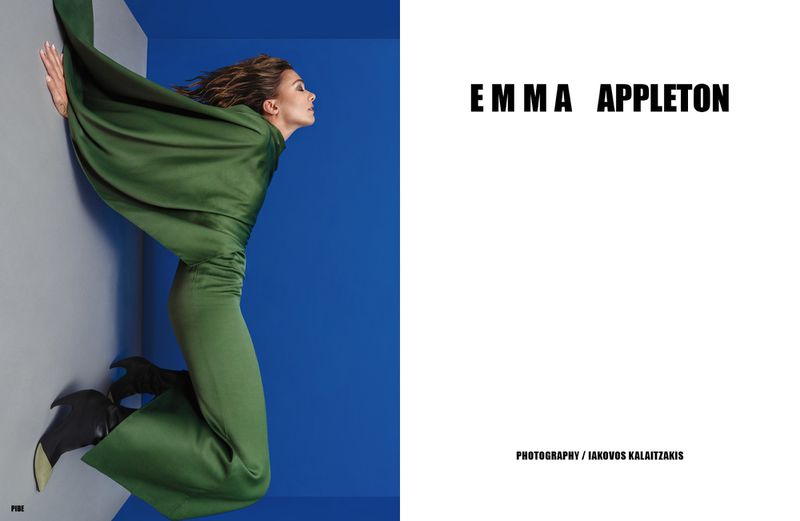 Fashion shot of a woman in a green dress leaning against a wall, with a minimalist blue and grey background, and visible magazine text.