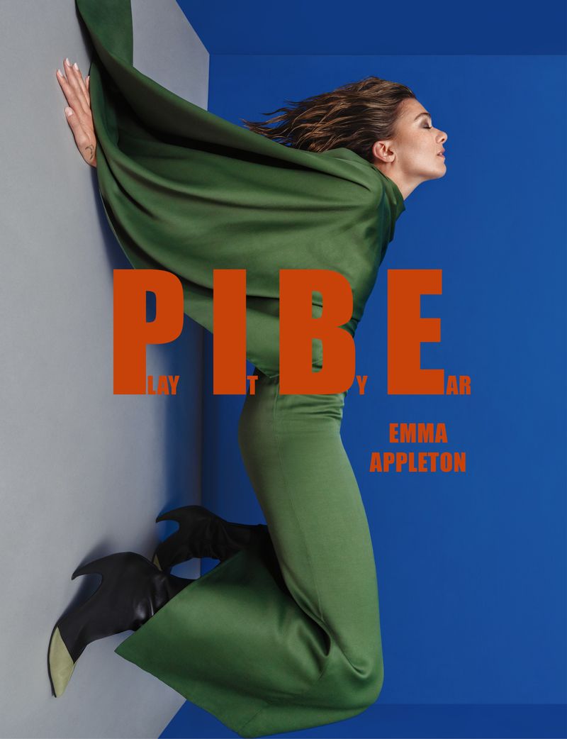 Emma Appleton poses in a green outfit with a large cape against a blue and grey backdrop, with a large orange text overlay.