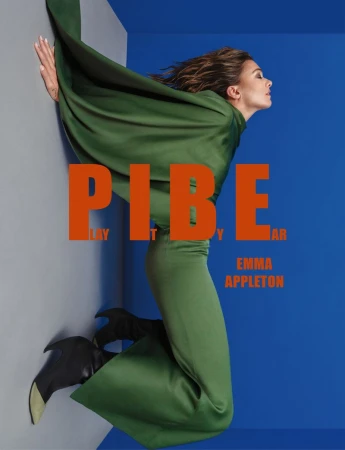 Emma Appleton wearing a long green dress and black heeled boots posed against a blue and grey studio background for a magazine cover