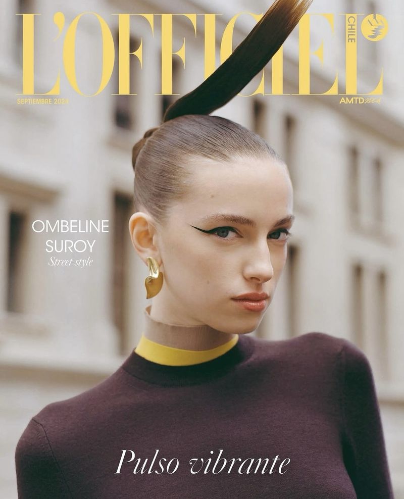 Fashion magazine cover featuring a model with sleek hair, wearing a brown top and yellow collar, posing against a blurred building backdrop.