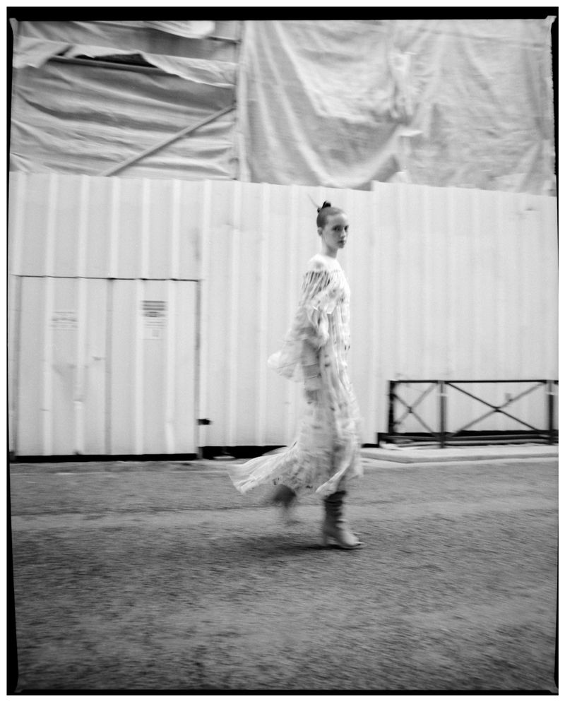 Model Ombeline Suroy walking on a city street in a flowing white dress and boots, captured in monochrome motion blur for L'Officiel Chile