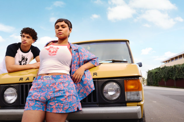 Two stylish people in front of a vintage yellow Range Rover with a blue sky background, modelling tropical print matching outfits.