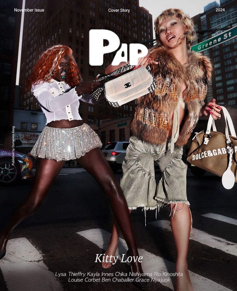 Two women pose with handbags on a city street in a fashion editorial with buildings in the background, shot at night for a magazine cover.