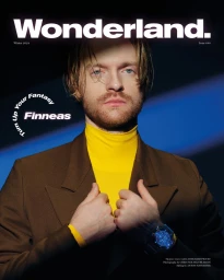 Portrait of Finneas wearing a brown blazer and yellow turtleneck against a dark blue background for Wonderland Magazine.