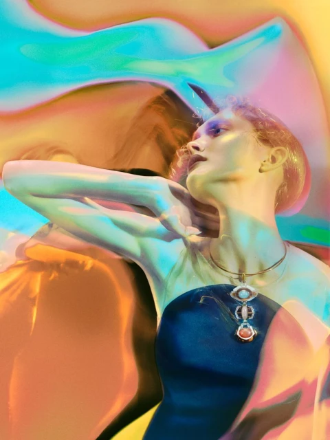 Woman with stylized makeup and jewelry in front of an abstract multicolored background with blue, orange, and green tones.