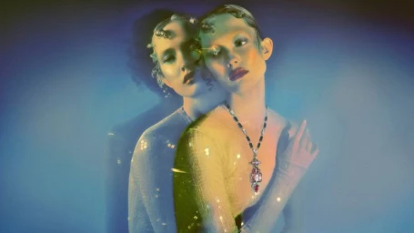 Model Viktoria Wirs wearing an ornate David Webb pendant necklace with an ethereal double exposure effect on a blue background.