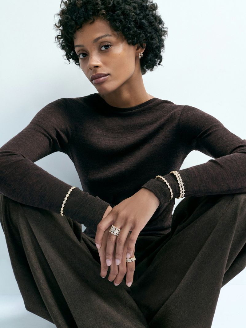 Elegant dark-skinned woman in long-sleeved brown top and trousers poses with jewelry. Simple, minimalist style portrait.
