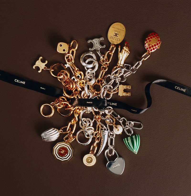 Accessorized Celine chain with assorted charms featuring logos and symbols, including a heart, dice, and Eiffel Tower, on a dark brown backdrop.