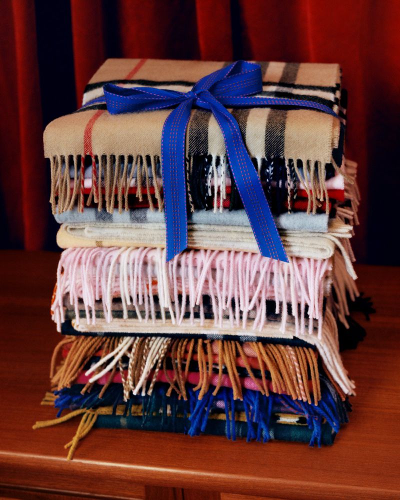 Stack of folded cashmere scarves in a variety of patterns tied with a blue ribbon, set against a red curtain backdrop.