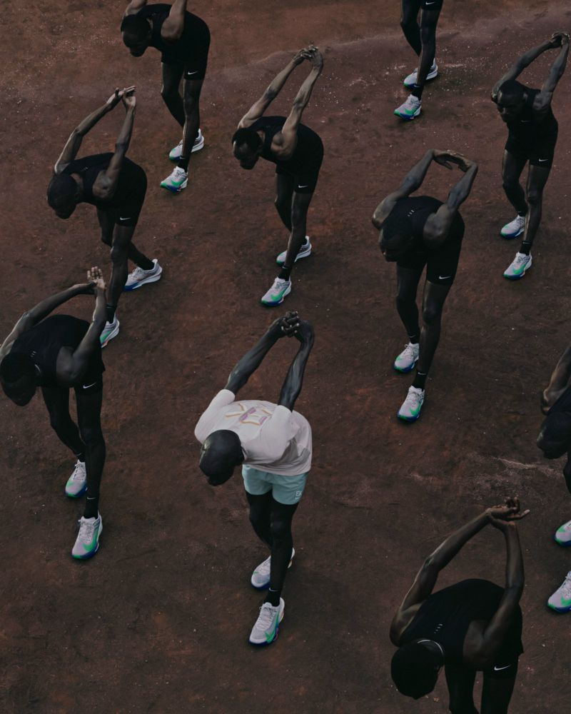 Aerial view of group of athletic dark-skinned men in running gear stretching arms overhead, showcasing fitness, training, and teamwork.