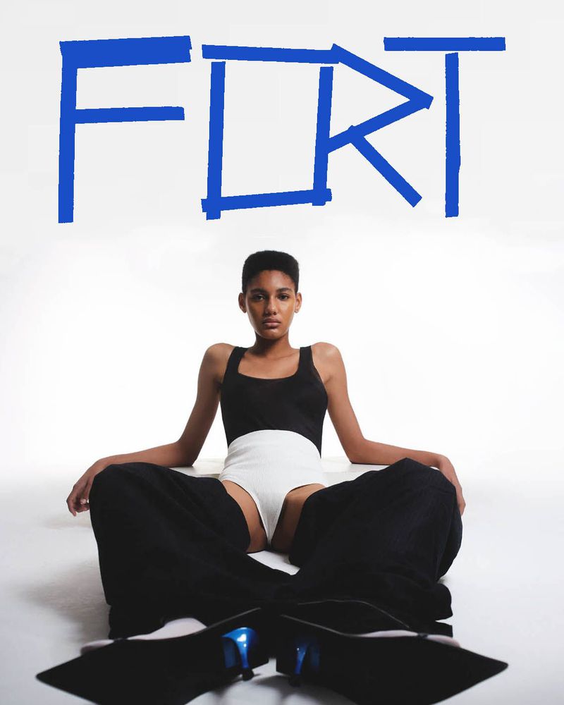 Fashion shot of a person in a black and white outfit sitting cross-legged on the floor, with large blue text art on a white background.