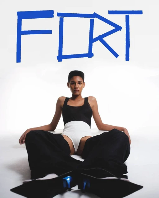 Fashion shot of a person in a black and white outfit sitting cross-legged on the floor, with large blue text art on a white background.