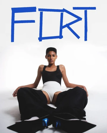 Fashion shot of a person in a black and white outfit sitting cross-legged on the floor, with large blue text art on a white background.
