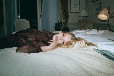 Blonde woman wearing a dark patterned dress lying on a bed in a hotel room