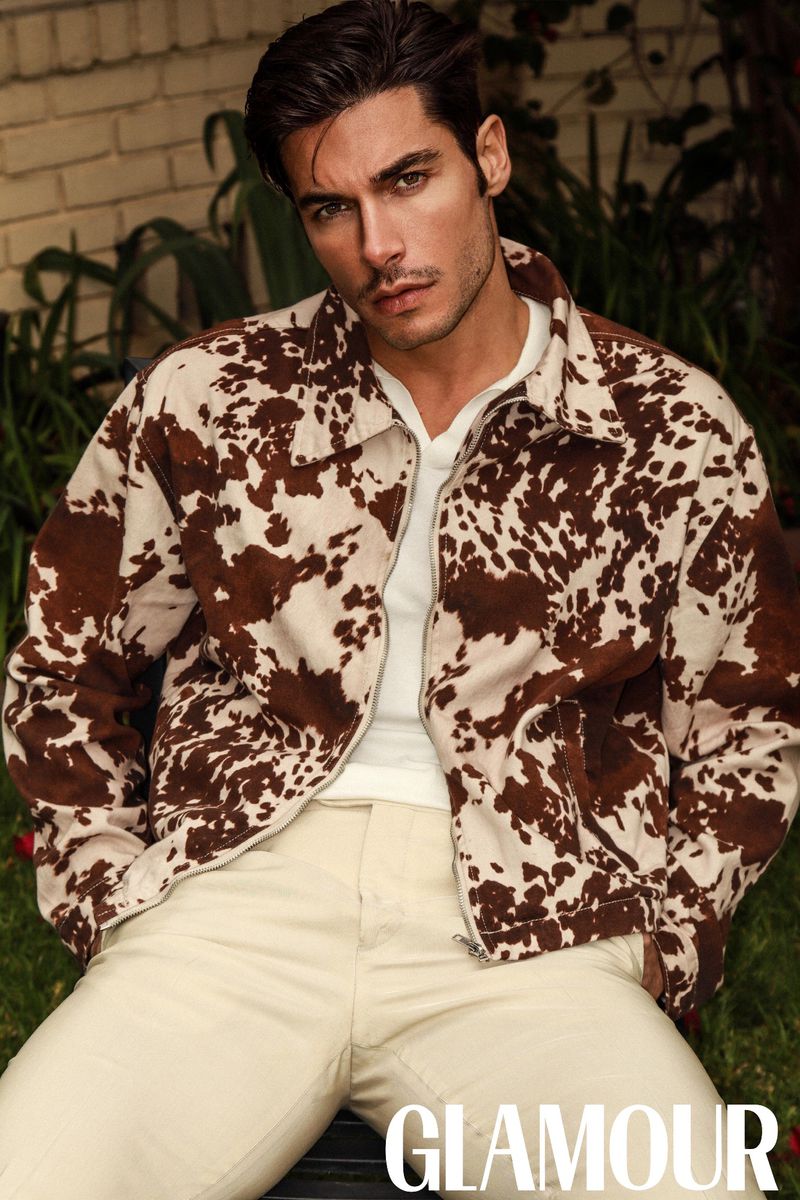 Portrait of male model Andrea Denver wearing a cow-print jacket and white t-shirt against a brick and garden background for Glamour Man Bulgaria.
